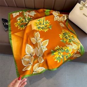 Orange floral square silk scarf with sunflower print and green border on leather background