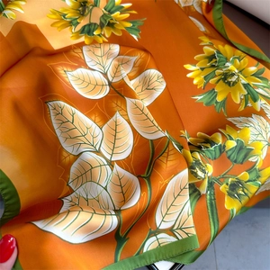 Close-up of luxury silk floral scarf featuring sunflower prints and vibrant green border