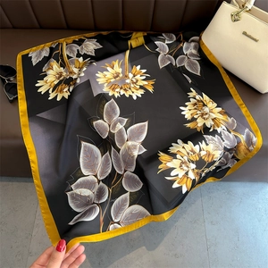 Detailed flat lay of black floral silk scarf with yellow border and elegant print