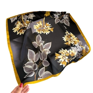 Elegant black floral silk scarf with yellow flower print and gold edges held in hand