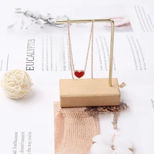 Dettaglio di una collana dorata con ciondolo a cuore rosso su supporto in legno