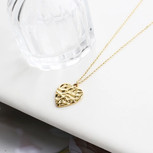 Detail shot of golden heart pendant with hammer-textured finish on stainless steel chain