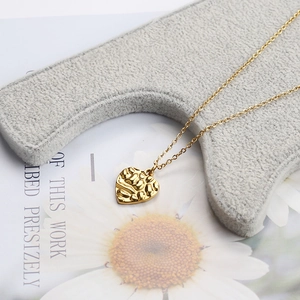 Close-up of golden heart pendant with hammer texture on elegant gray display stand