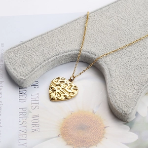Detail of gold heart pendant with hammered texture on a gray velvet jewelry display stand