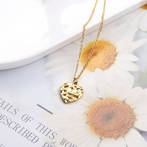 Macro shot of gold heart pendant with hammered texture on a white tray with daisies