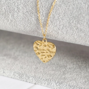 Macro detail of golden hammered heart pendant showing unique textured finish on a chain