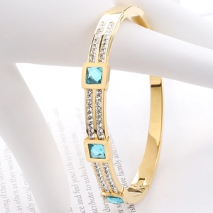 Detailed close-up of a gold-plated bangle with blue square gems and rows of small zircons