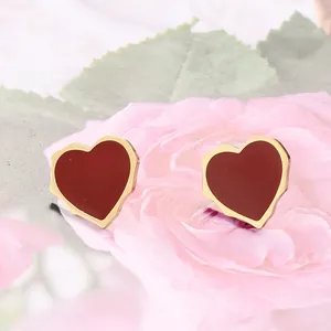 Gros plan de boucles d'oreilles cœur dorées en émail rouge sur fond de fleurs roses