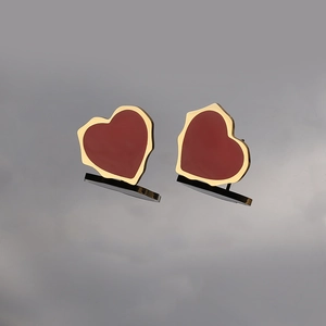 Vue macro de boucles d'oreilles cœur dorées irrégulières avec émail rouge foncé