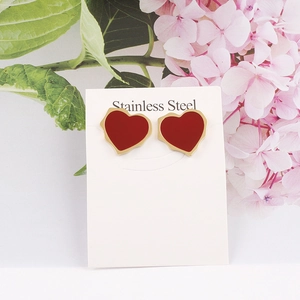 Gros plan de boucles d'oreilles cœur rouge en acier inoxydable sur carte avec fleurs