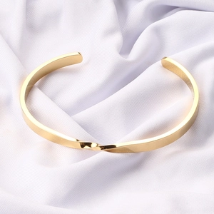 Macro shot of gold Mobius knot cuff bracelet with polished finish on white fabric