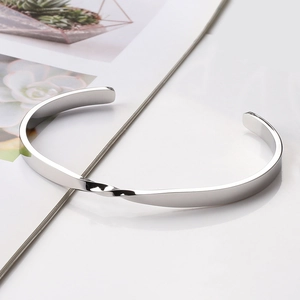 Close-up of silver Mobius twist cuff bracelet made of polished stainless steel on white surface