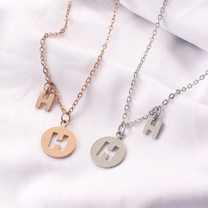 Minimalist H-letter necklace in silver and rose gold finishes on white fabric background