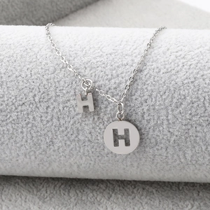 Macro detail of silver stainless steel sunflower and letter H pendants on a necklace