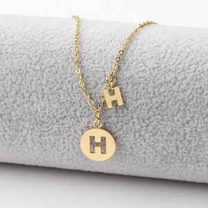 Close-up of golden stainless steel H-letter pendant necklace on a grey velvet display