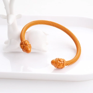 Macro detail of mustard yellow twisted rope bangle with decorative acorn finials