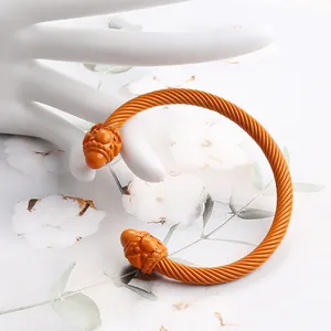 Detail of orange enamel cable cuff with intricate engraved end caps on a jewelry hand display