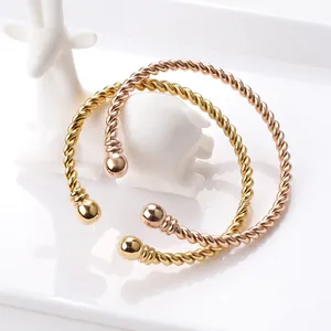 Detail of twisted cable cuff bangles in gold and rose gold finish with ball ends