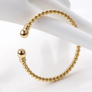 Close-up of golden twisted wire cuff bangle featuring spherical ball ends on a hand model