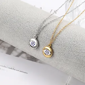 Detail of gold and silver evil eye pendants with blue enamel on a soft grey display stand