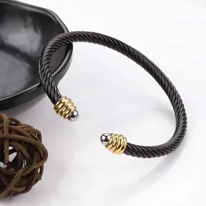 Detail of twisted black stainless steel cable bracelet with gold and silver end caps