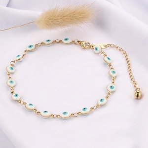 Dettaglio della cavigliera Evil Eye dorata con smalto bianco e campanellino su tessuto