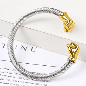Macro detail of silver twisted cable bracelet with golden fist ends on white stand