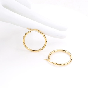 Macro detail of gold-plated twisted rope hoop earrings on a ceramic hand stand