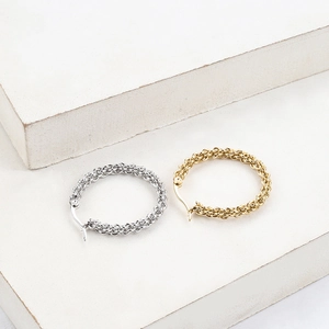 Detail of woven chain link gold and silver hoop earrings on a stone background