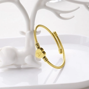 Détail d'un bracelet câble doré avec breloque cœur gravée de la lettre A sur un support