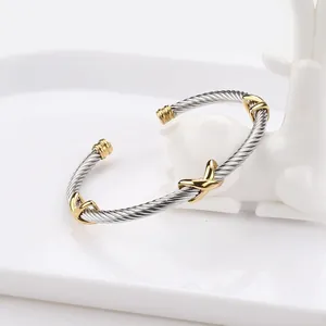 Macro shot of silver steel cable bracelet featuring three golden crisscross X details