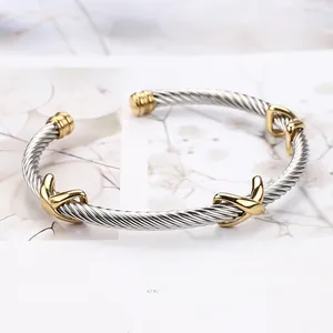 Macro shot of silver cable wire cuff bracelet featuring golden X-shaped accents and finials
