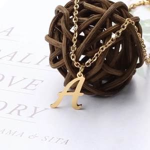 Detail of a polished gold cursive letter A pendant anklet on a white artistic card