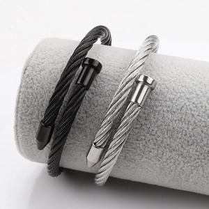 Détail macro des bracelets câbles torsadés en acier noir et argent sur support de bijoux