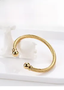 Detailed close-up of a gold twisted cable cuff bracelet with round bead tips on a tray