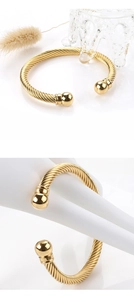 Detail of gold twisted cable cuff bracelet with spherical ends and polished metallic finish