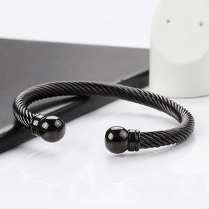 Macro detail of black cable twist bangle with polished metal balls on white surface