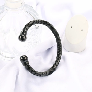 Detail of black twisted cable cuff bracelet with spherical ends on white silk