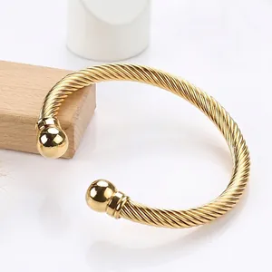 Polished gold twisted cable stainless steel cuff bangle with spherical end caps on white