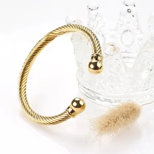 Detail of a gold twisted cable cuff bangle with polished beads on a luxury crown stand