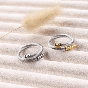 Detailed view of cable twisted steel rings with zircon accent on beige velvet surface