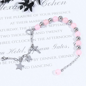 Bracelet en perles roses avec breloques croix et cœur argent sur carte blanche