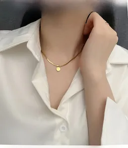 Détail d'un collier chaîne serpent dorée avec un pendentif disque rond poli chic