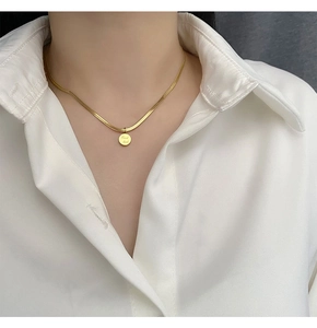 Détail d'un collier chaîne serpent dorée avec pendentif rond gravé Good Luck