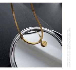 Gros plan sur collier chaîne serpent dorée avec pendentif rond gravé Good Luck