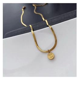 Gros plan d'un collier chaîne serpent dorée avec pendentif pièce gravé Good Luck