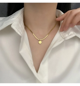 Gros plan d'un collier chaîne serpent dorée avec pendentif Good Luck porté par un mannequin