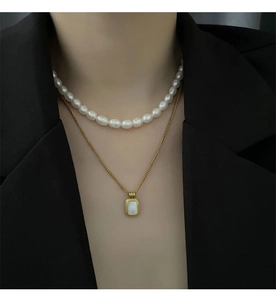 Close-up of layered gold necklace with white freshwater pearl and shell pendant on model