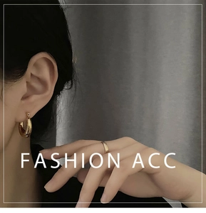 Detail showing chunky gold hoop earrings and minimalist ring set on textured background