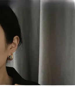 Close-up of golden C-shaped hoop earrings with textured wave engraving on a model ear